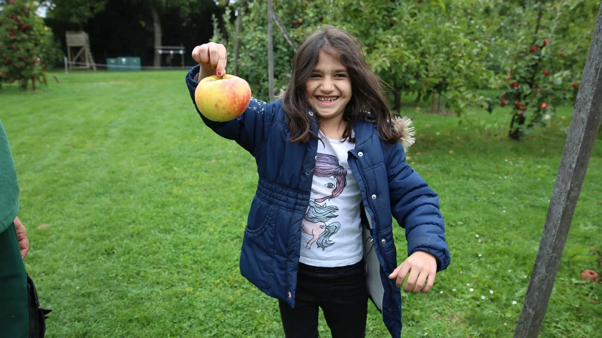 Ausflug zum Apfelhof: Inmitten von Apfelbäumen hält ein Kinden einen besonders großen Apfel hoch.