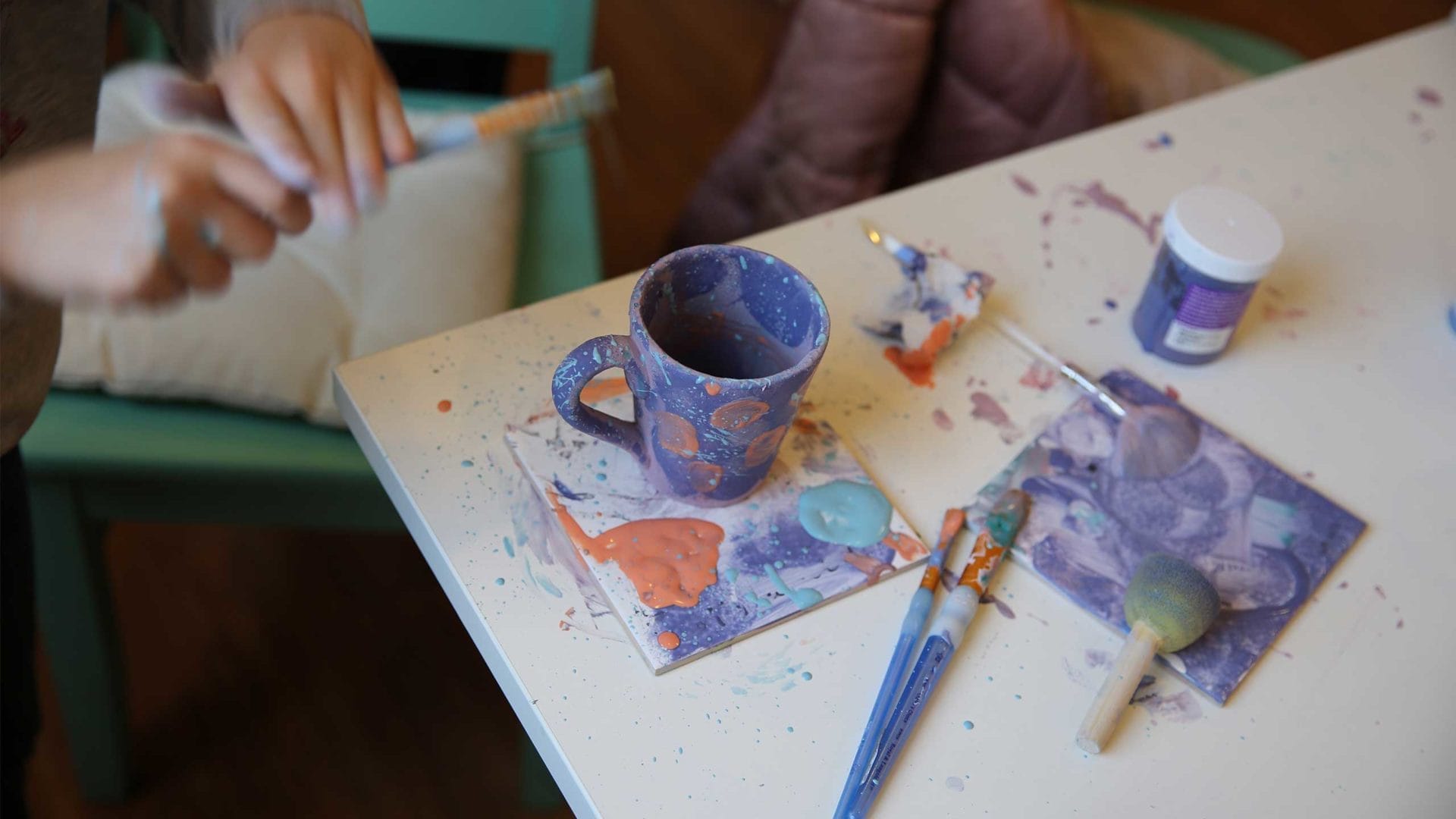 a cup on a table of the creative workshop with brushes and dabs of paint