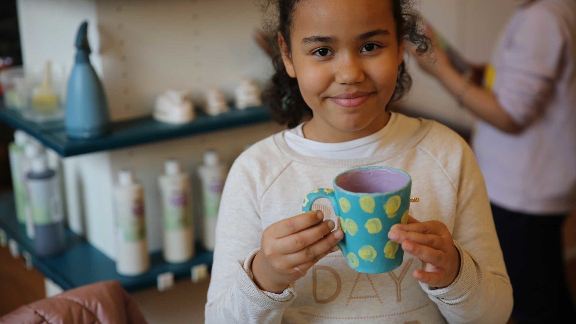 Ein Kind aus der Arche Frankfurt mit einer selbstgemachten Tasse in der Hand steht in der Kreativwerkstatt