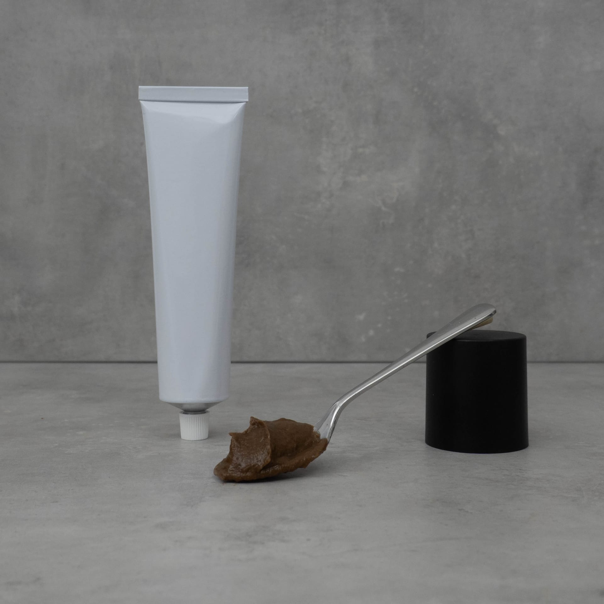 A spoonful of Tasty Paste in front of an upside-down tube